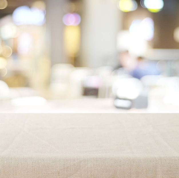 Ripiano del tavolo vuoto con la tovaglia di tela sopra il caffè vago con il fondo del bokeh