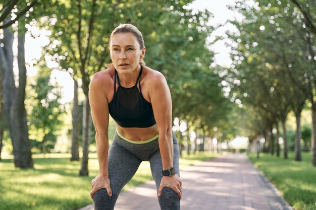 Riposa per un po' bella donna sportiva in abbigliamento sportivo facendo una pausa mentre fa jogging in un parco verde