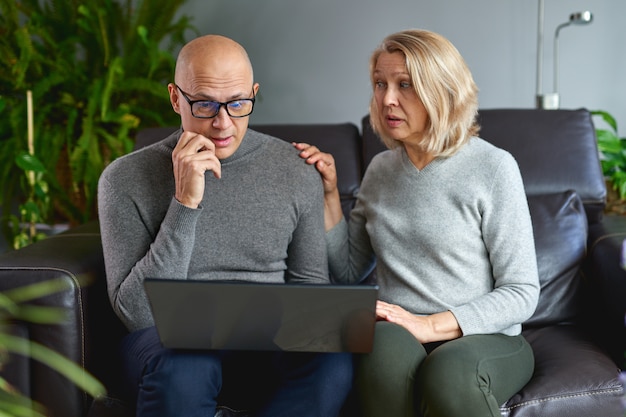 Riposo di mezza età della mamma in salotto con il fine settimana della famiglia di computer di uso del bambino adulto insieme.