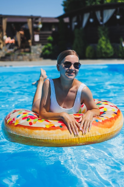 Riposo in piscina Felice giovane donna in costume da bagno occhiali da sole e anello di gomma gonfiabile che galleggia nell'acqua blu Vacanze estive di lusso nella piscina del resort termale