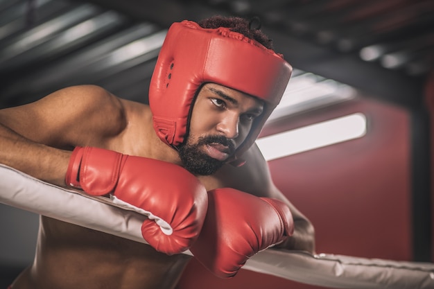 Riposo. Kickboxer dalla pelle scura in un casco rosso che riposa dopo il combattimento