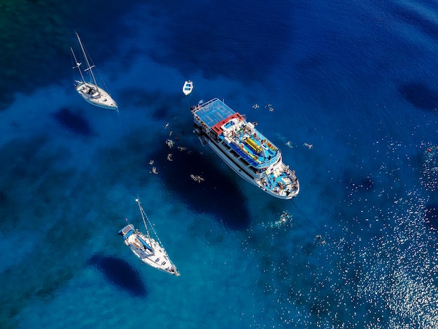 Ripresa aerea della bellissima laguna blu al caldo giorno d'estate con barca a vela. La vista dall'alto delle persone nuota intorno alla barca.