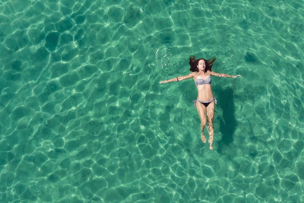 Ripresa aerea di una bella donna vestita in bikini che galleggia in un'acqua turchese tropicale.