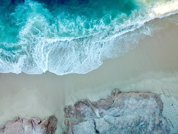 Ripresa aerea di una spiaggia soleggiata con acqua blu e rocce