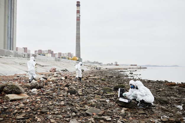 Ripresa grandangolare di lavoratori che indossano tute ignifughe che raccolgono campioni di sonde dall'acqua in un'area industriale...