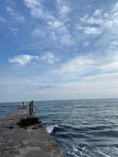 Ripresa verticale di un pescatore irriconoscibile in piedi su un molo, che pesca in mare