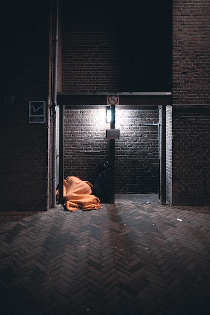 Ripresa verticale di un senzatetto che dorme sotto una coperta arancione di fronte a un edificio