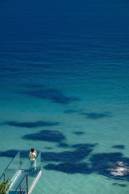 Ripresa verticale di una persona che guarda il mare da un balcone di vetro in una giornata di sole