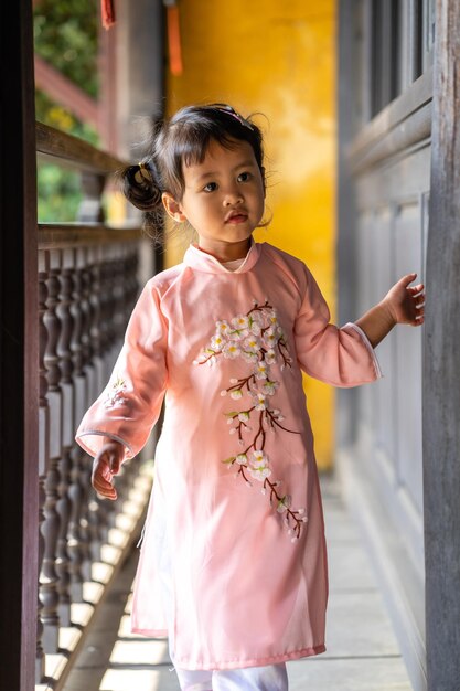 Ripresa verticale di una simpatica bambina vietnamita in un ao dai rosa che cammina su un vecchio balcone di legno