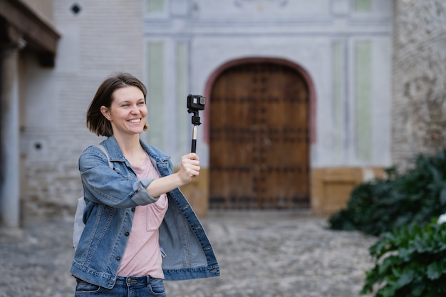 Riprese della ragazza del viaggiatore soddisfatte della macchina fotografica di azione. Giovane donna attraente che cammina sulla strada godendo il suo tempo di vacanza.