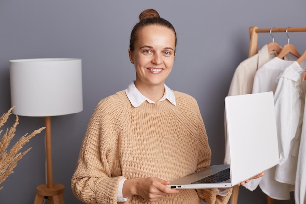 Riprese in interni di una donna caucasica soddisfatta sorridente che tiene il laptop in mano lavorando online facendo shopping vendendo abiti eleganti guardando la fotocamera con un sorriso a trentadue denti