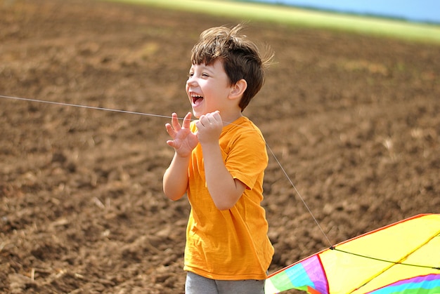 Risate e sorrisi felici del bambino che giocano con l'aquilone di volo al giorno di estate soleggiato al campo