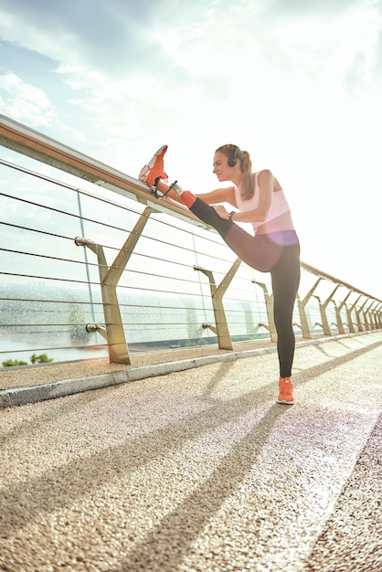 Riscaldamento prima della corsa vista laterale della donna positiva disabile in abbigliamento sportivo e allungamento delle cuffie