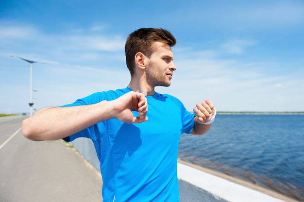 Riscaldarsi prima di fare jogging. Bel giovane che si esercita stando in piedi all'aperto