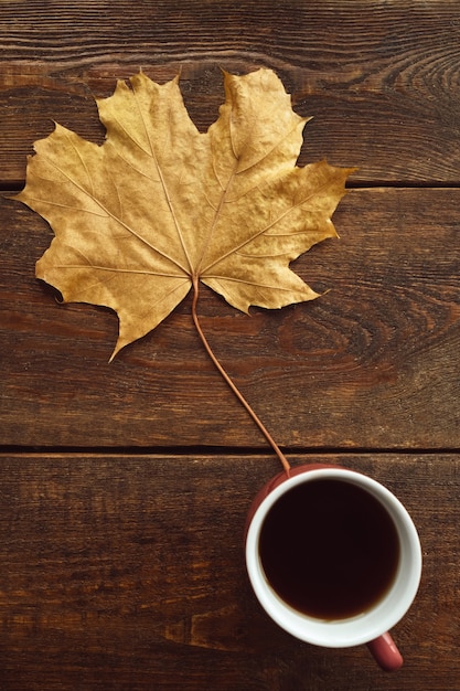 Riscaldati con il caffè nero in autunno. Foglia di acero sulla parete di legno rustica