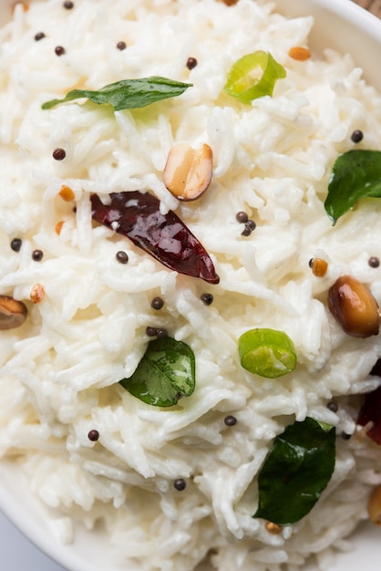 Riso cagliato o Dahi Bhat O Chawal con foglia di curry, arachidi e peperoncino- Servito in una ciotola su sfondo lunatico. Messa a fuoco selettiva