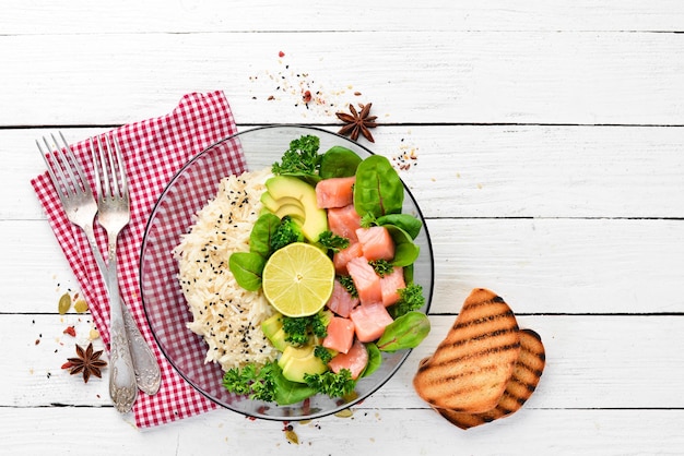 Riso con salmone, avocado e spinaci In un piatto nero su sfondo di legno Vista dall'alto Spazio libero per il testo Disposizione piatta