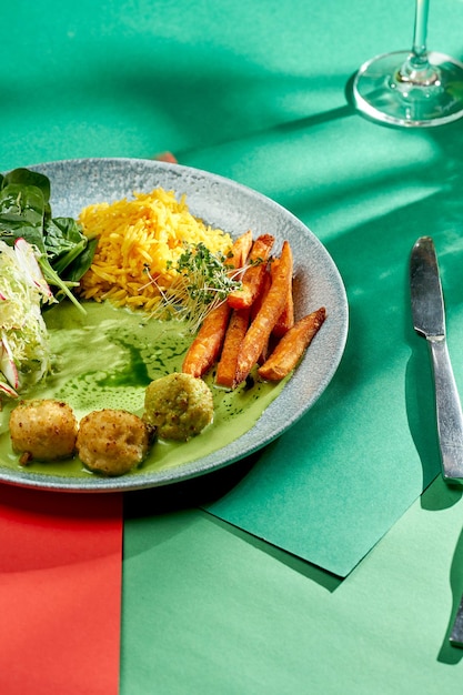 Riso indiano al curry con salsa verde, patate dolci e polpette in un piatto di sfondi luminosi. Messa a fuoco selettiva, luce dura