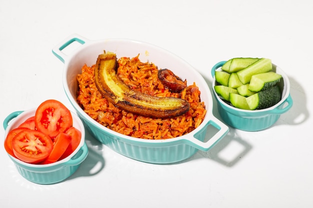 Riso Jollof con banana fritta Verdure fresche pomodoro e cetriolo Sfondo bianco Riso tradizionale nigeriano con pomodori cipolle e spezie