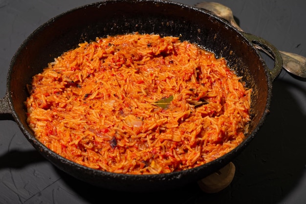 Riso Jollof in padella su sfondo scuro Un piatto tradizionale nigeriano di riso, pomodori e spezie