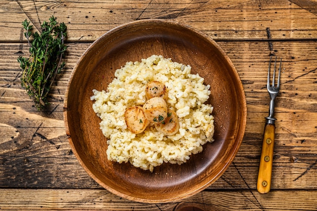 Risotto all'italiana con capesante in padella. fondo in legno. Vista dall'alto.