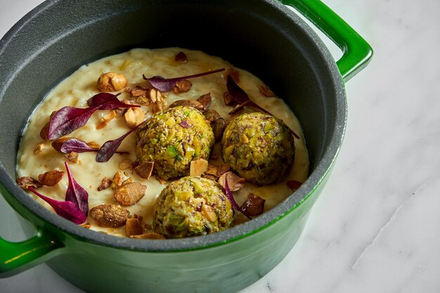 Risotto cremoso con polpette di sedano, arachidi e foglie di basilico in una pentola verde su marmo bianco