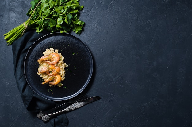 Risotto italiano con gamberi su un piatto nero, un mazzetto di coriandolo.