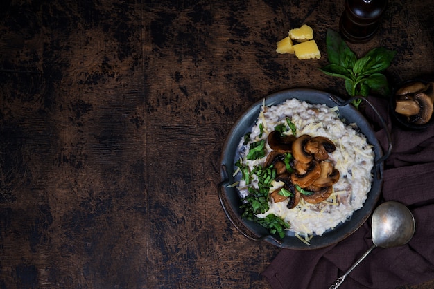 Risotto Piatto Italiano Con Funghi, Parmigiano Ed Erbe. Risotto in un piatto di rame su uno sfondo marrone di legno