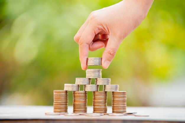 Risparmio di denaro mano mettendo le monete in pila sul tavolo con il sole. concetto di finanza e contabilità