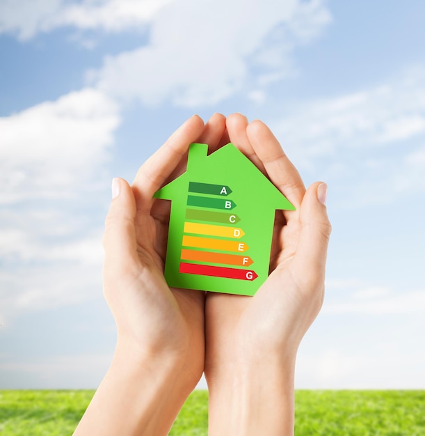 risparmio energetico, immobiliare e concetto di casa di famiglia - primo piano di mani femminili che tengono una casa di carta verde con valutazione di efficienza energetica
