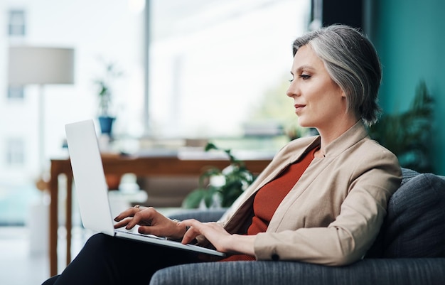 Rispondere alle e-mail Foto ritagliata di un'attraente donna d'affari matura seduta da sola e che utilizza un laptop nel suo ufficio a casa