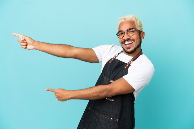 Ristorante cameriere colombiano uomo isolato su sfondo blu che punta il dito sul lato e presenta un prodotto