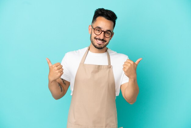 Ristorante cameriere uomo caucasico isolato su sfondo blu con il pollice in alto gesto e sorridente