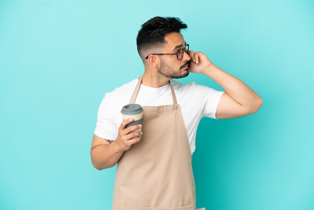 Ristorante cameriere uomo caucasico isolato su sfondo blu tenendo il caffè da asporto e un mobile