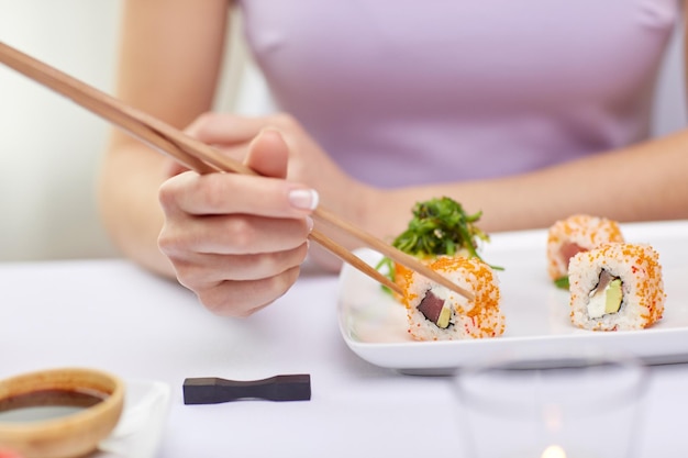 ristorante, cibo, persone, cucina asiatica e giapponese concetto - primo piano di donna che mangia sush con le bacchette al ristorante