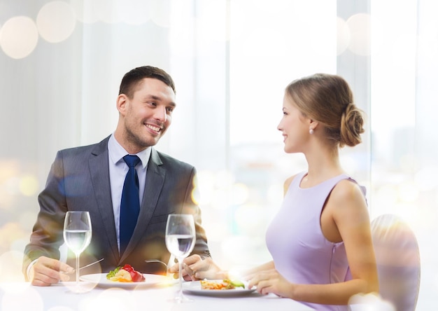 ristorante, coppia e concetto di vacanza - coppia sorridente che mangia piatto principale al ristorante