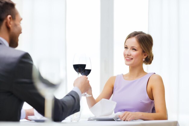 ristorante, coppia e concetto di vacanza - giovane donna sorridente con un bicchiere di vino rosso guardando il fidanzato o il marito al ristorante