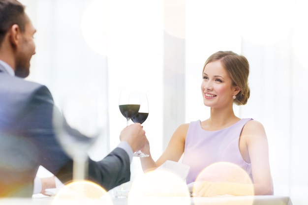 ristorante, coppia e concetto di vacanza - giovane donna sorridente con un bicchiere di vino rosso guardando il fidanzato o il marito al ristorante