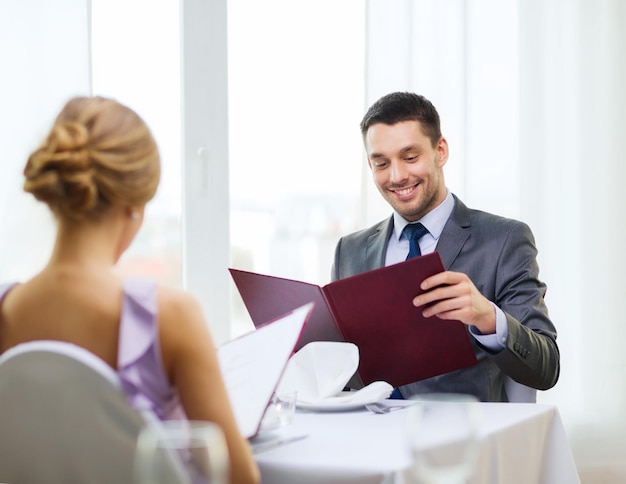 ristorante, coppia e concetto di vacanza - giovane sorridente guardando il menu al ristorante