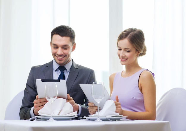 ristorante, coppia, tecnologia e concetto di vacanza - coppia sorridente con menu su computer tablet pc al ristorante