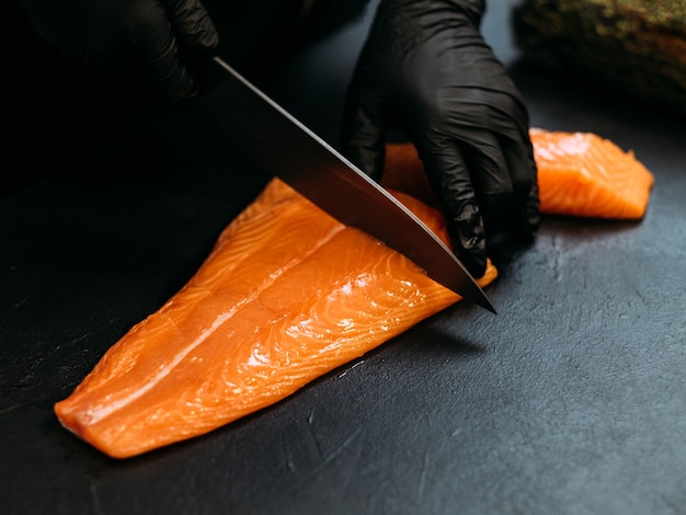 Ristorante di pesce. Primo piano delle mani dello chef usando il coltello per tagliare il filetto di salmone fresco.