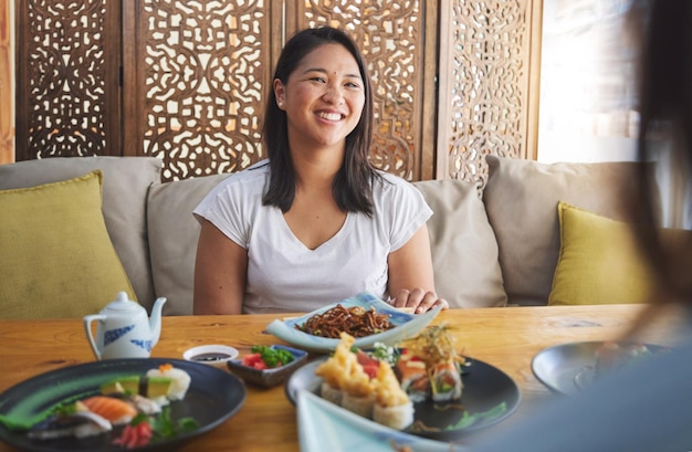 Ristorante di sushi e cibo giapponese con una donna che sorride con noodles e piatto di pesce Pranzo di una donna asiatica affamata e pasto cinese con un amico felice di aver legato e mangiato insieme a un tavolo