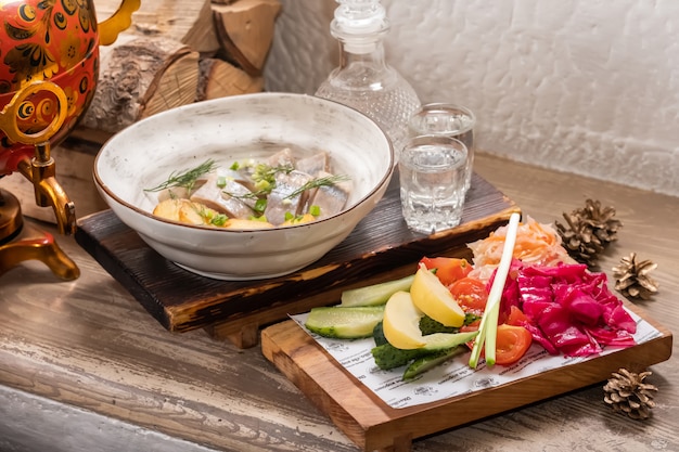 Ristorante Menu di pesce con aringhe salate con anelli di cipolla e patate a cubetti bollite su un elegante piatto da ristorante con set di vodka fredda alcolica e salamoia assortita.