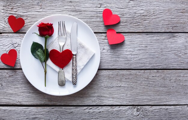 ristorante tavolo in legno con cuore e rosa con posate sul piatto