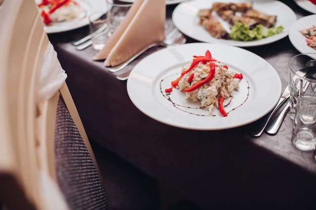 Ristorazione per matrimoni. Piatto in ceramica bianca con gustosa insalata con pepe rosso in primo piano.