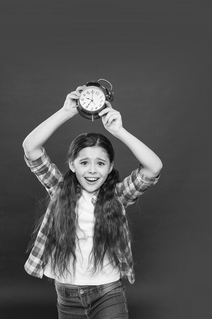 Risveglio ragazzo adolescente che mostra il tempo sull'orologio ragazza sensazione di felicità bambino essendo in tarda mattinata gestione del tempo orologio meccanico retrò periodo di giorno del sonno programma per bambini spazio di copia