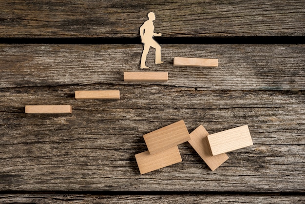 Ritagli di sagoma di un uomo che cammina su gradini in legno con domino sulla vecchia superficie del tavolo in legno grezzo.