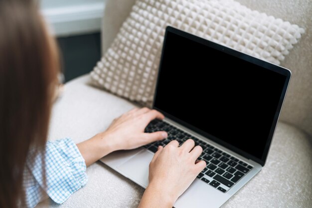 Ritaglia la foto di una giovane donna che lavora su un computer portatile seduto su un tappeto a casa