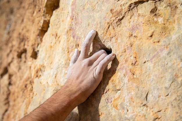 Ritaglia la mano maschile in polvere di gesso bianca appesa su roccia ruvida mentre si arrampica