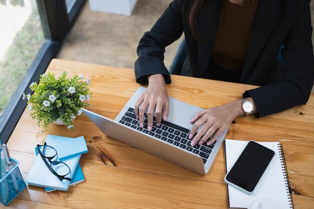 Ritagliata colpo di donna d'affari che lavora con il computer portatile sulla scrivania in legno.